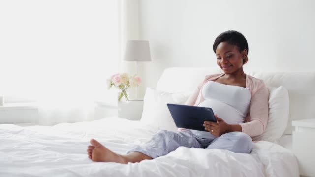 happy-pregnant-woman-with-tablet-pc-in-bed