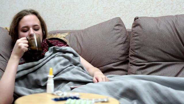 Teen-girl-drinking-medicine-tea-warm.-Lying-on-the-couch-with-a-smartphone