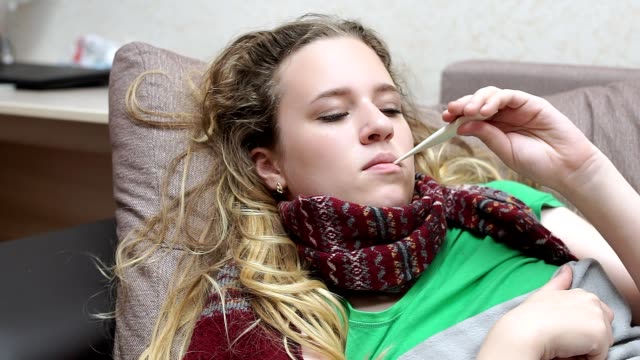 Teenager-Mädchen-misst-ihre-Temperatur,-verärgert-schaut-das-Fieberthermometer