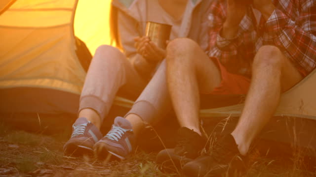 Friends-in-comfortable-shoes-sitting-in-tent-and-drinking-tea,-hiking-in-forest