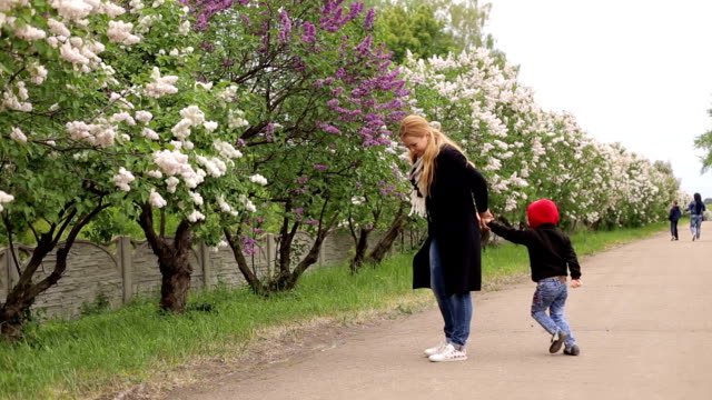 Ein-kleiner-Junge-läuft-um-seine-Mutter-im-Frühjahr-Park-unter-den-blühenden-Bäumen