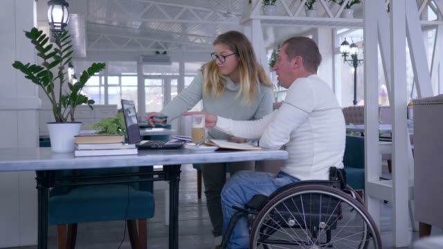 enseñanza-para-hombre-mayores-discapacitados,-feliz-estudiante-enfermo-en-silla-de-ruedas-con-la-mujer-de-la-educador-hogar-estudiar-usando-la-computadora-portátil