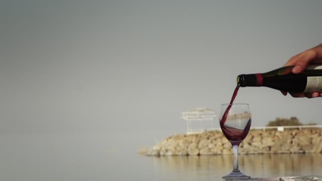 Rot-Wein-gießen,-Zeitlupe,-männliche-Hand-gießt-Wein-am-Meer