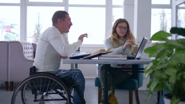 Educación-para-hombre-senior-estudiante-con-discapacidad,-enfermos-en-silla-de-ruedas-con-las-mujeres-de-tutor-durante-cursos-de-la-enseñanza-página-uso-de-ordenador-portátil