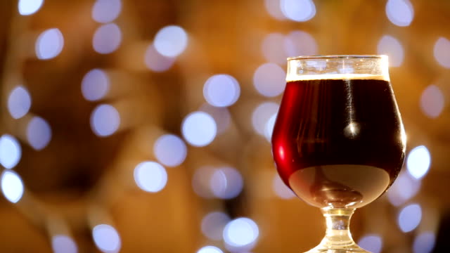 Cold-delicious-dark-beer-in-a-glass-is-spinning-on-background-of-blurred-lights.-Craft-Beer-close-up-rotation.-Pint-of-beer.-Pub-concept