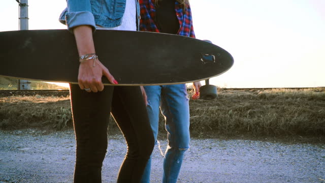 zwei-schöne-und-junge-Frauen-gehen-und-sprechen-mit-skateboard