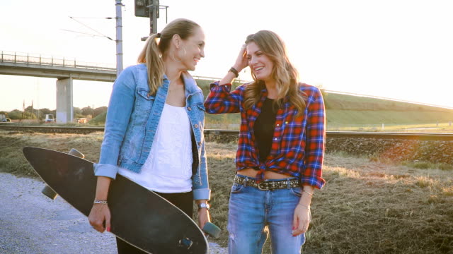 zwei-schöne-und-junge-Frauen-gehen-und-sprechen-mit-skateboard
