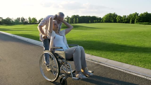 Älteres-Paar-mit-Frau-im-Rollstuhl-spazieren