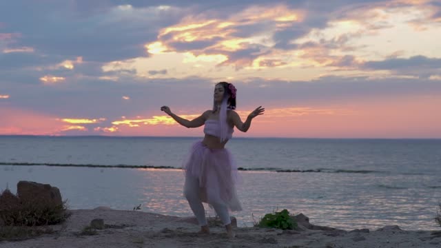 Cute-girl-with-sparkling-makeup-in-a-pink-dress-dancing-on-the-bank-of-the-river.-The-dance-of-a-sensual-woman-with-a-wonderful-hairstyle-with-flowers.-Slow-motion.