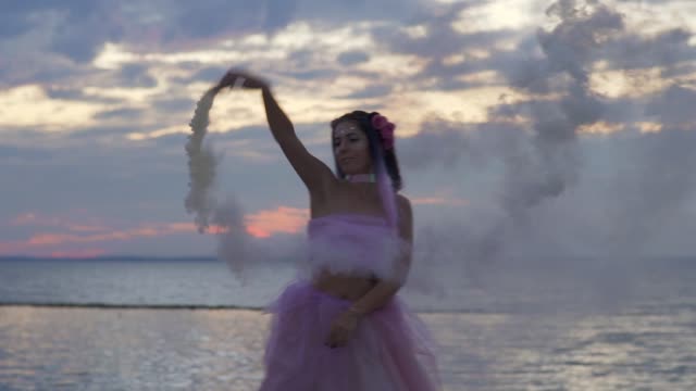Zartes-Mädchen-mit-funkelnden-Make-up-in-einem-rosa-Kleid-tanzen-mit-Rauchbomben-am-Ufer-des-Flusses.-Der-Tanz-einer-sinnlichen-Frau-mit-einer-wunderschönen-Frisur-mit-Blumen.-Slow-Motion.