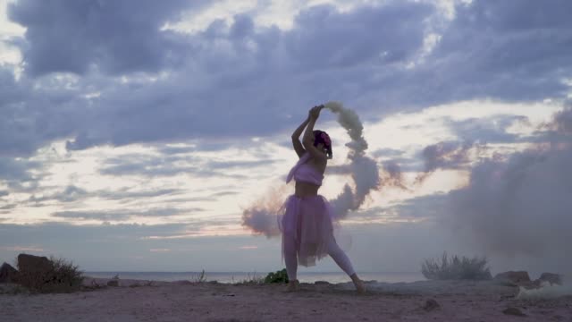 Beautiful-young-woman-with-bright-makeup-in-a-pink-dress-dancing-with-smoke-bombs-outdoors.-The-dance-of-a-sensual-girl-with-a-wonderful-hairstyle-with-flowers.-Slow-motion.