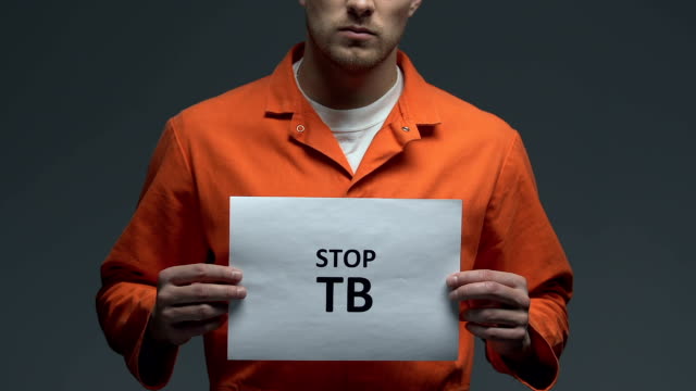 Stop-TB-phrase-on-cardboard-in-hands-of-Caucasian-prisoner,-healthcare-need