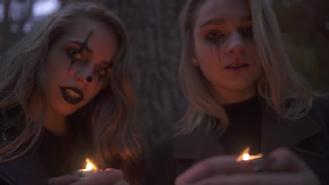 Zwei-junge-blonde-Mädchen-mit-furchterregenden-Halloween-Make-up-halten-kleine-Kerzen-in-den-Händen-und-Blick-in-die-Kamera.