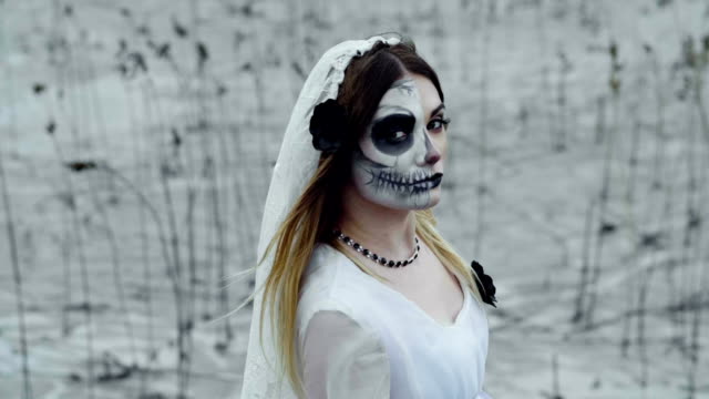 Eine-Frau-mit-gruseligem-Make-up-für-Halloween-in-einem-weißen-Brautkleid.-zeitlupe.-Hd
