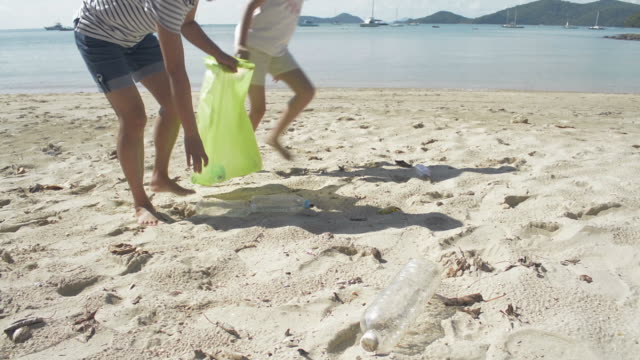 Mamá-y-su-hija-recogiendo-basura-en-la-playa-de-arena-en-una-bolsa-de-plástico-verde,-las-botellas-de-plástico-se-recogen-en-la-playa,-los-voluntarios-limpiando-la-playa.