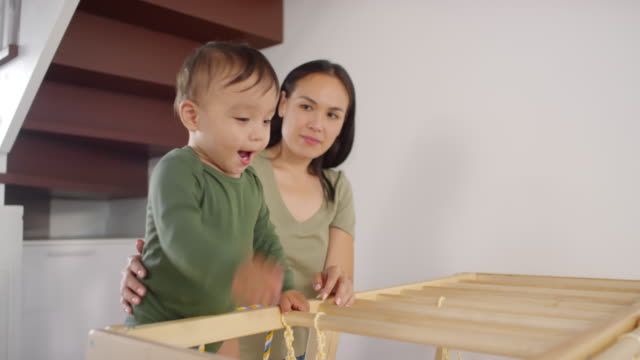 Asiatische-Mutter-beobachten-Kleinkind-spielen-auf-Kletterrahmen-zu-Hause