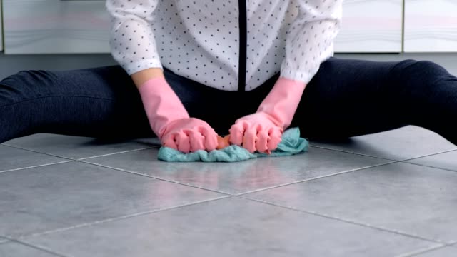 Woman-in-pink-rubber-gloves-washes-and-rubs-hard-the-stain-on-kitchen-floor-with-a-cloth.-Gray-tiles-on-the-floor.-Hands-close-up.