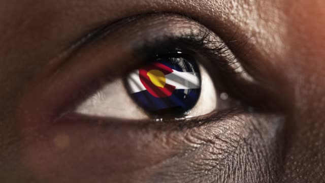 Mujer-ojo-negro-en-primer-plano-con-la-bandera-del-estado-de-Colorado-en-iris,-estados-unidos-de-América-con-movimiento-de-viento.-concepto-de-vídeo
