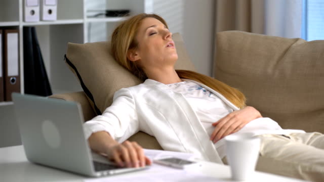 Müde-Geschäftsfrau-schlafend-auf-der-Couch-im-Büro-mit-Laptop-und-Telefon