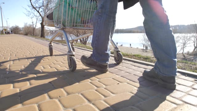 Rear-view-of-homeless-man's-legs-walking-with-cart