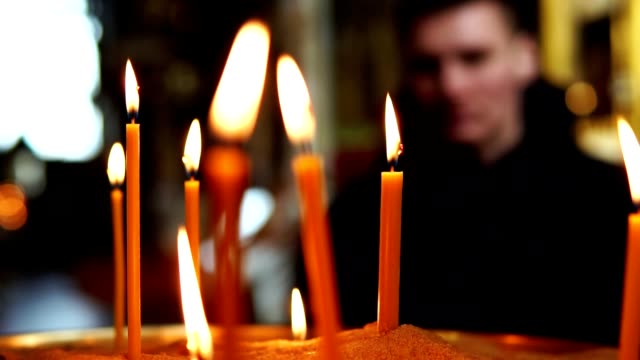 The-man-looks-at-the-burning-candles-in-the-focus,-slow-motion