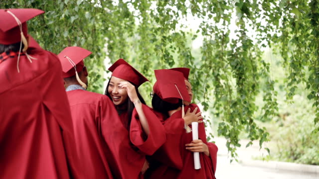 Slow-Motion-von-fröhlichen-Menschen-umarmen-einander-nach-Abschlussfeier-hält-Diplome-und-traditionellen-Hüte-und-Kleider-tragen.-Aufregung-und-Feier-Konzept.