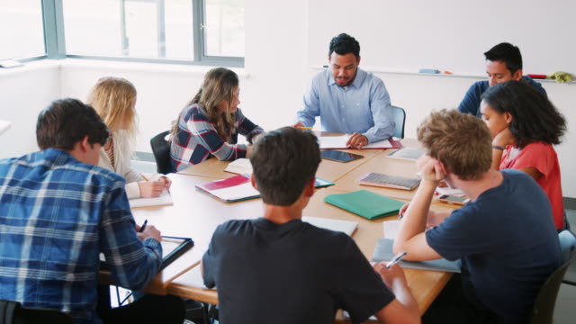 Gruppe-von-Schülerinnen-und-Schüler-mit-männlichen-Lehrer-arbeiten-am-Schreibtisch
