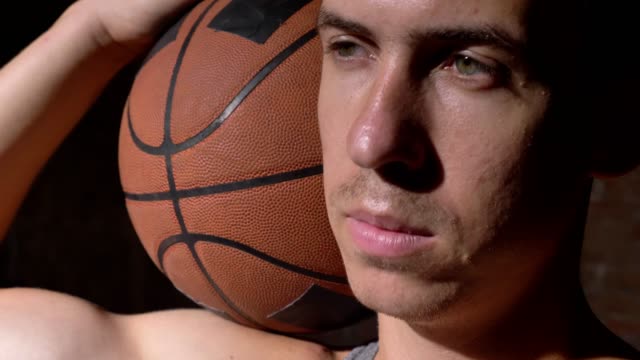 Serious-basketball-player-holding-ball-on-his-shoulder-and-looking-sideways