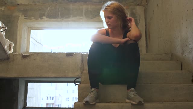 Unglückliche-Mädchen-sitzt-auf-der-Treppe-in-einem-verlassenen-Gebäude
