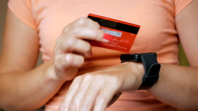 Mujer,-compra-online-con-tarjeta-de-crédito-en-reloj-inteligente.-Consumo-compras-online-por-internet.-Chica-es-pagar-con-un-reloj-elegante.-Compras-en-línea-con-el-smartwatch-y-una-tarjeta-de-crédito-en-la-mano.