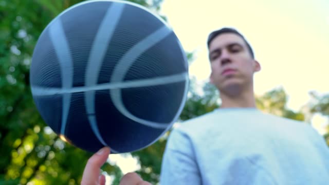 Young-man-spinning-basketball-on-one-finger-in-park,-outdoor-court,-low-angle