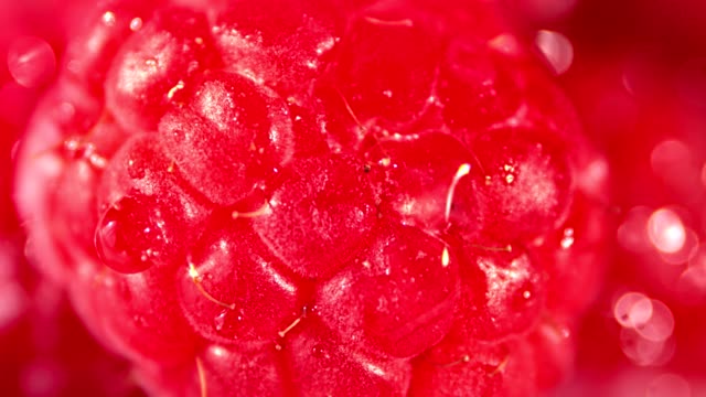 Macro-shot-stream-of-clear-pure-water-falling-on-beautiful-red-raspberry-reflecting-light