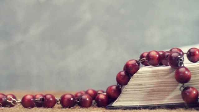 Open-Bible-and-the-crucifix-beads-on-a-golden-table,-close-up.-Beautiful-dark-background.-Religion-concept