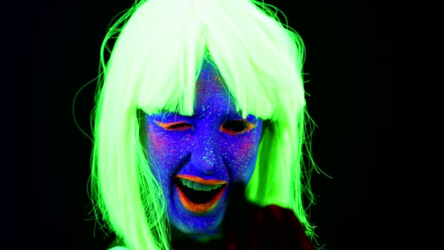 Woman-with-UV-face-paint,-wig,-glowing-clothing-dancing-in-front-of-camera,-face-close-up-of-make-up.-Caucasian-woman.-.