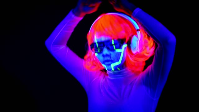 Mujer-con-pintura-Ultravioleta-de-la-cara-de-cyborg,-peluca,-brillantes-gafas,-ropa-bailando-y-escuchando-música-con-auriculares.-Mujer-asiática.-.