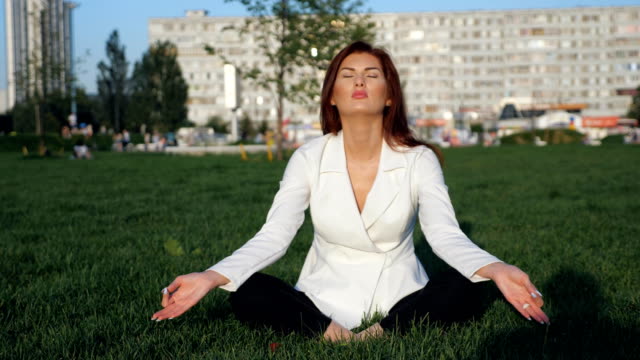 Hermosa-empresaria-en-traje-blanco-haciendo-yoga-para-relajarse-al-aire-libre,-lenta
