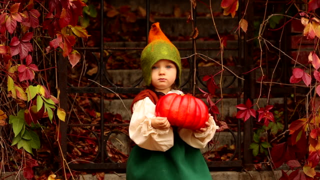 Cute-girl-in-a-gnome-costume-holds-a-pumpkin-for-Halloween