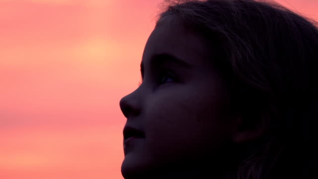 Kid-looking-up-at-the-sky-in-nature.-Little-girl-praying-looking-up-at-purple-sky-with-hope,-close-up.