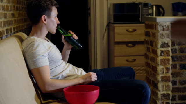 Man,-football-fan-is-drinking-beer-and-chips-in-front-of-TV