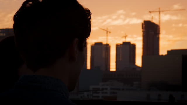 Rückansicht-des-Paares-auf-auf-dem-Dachterrasse-mit-Blick-über-Stadt-Skyline-bei-Sonnenuntergang