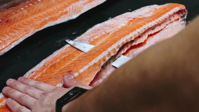 Chef-takes-out-bones-from-the-salmon-fillet,-cutting-fish-on-slices-for-cooking-sushi-in-4k-resolution-in-slow-motion