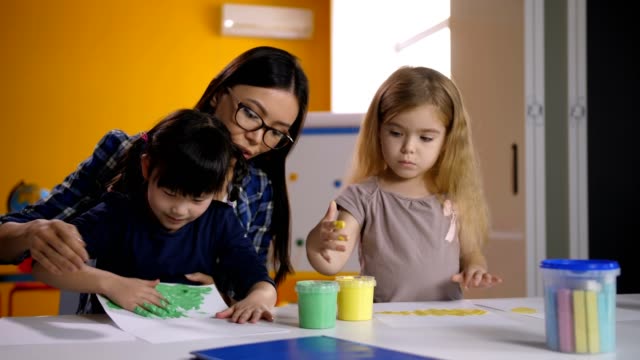 Diverse-kids-with-teacher-hand-painting-in-class