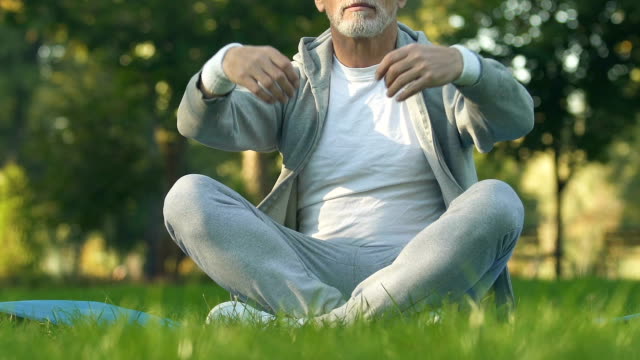 Mature-sportive-man-sitting-in-lotus-position-in-park,-recreation-and-meditation