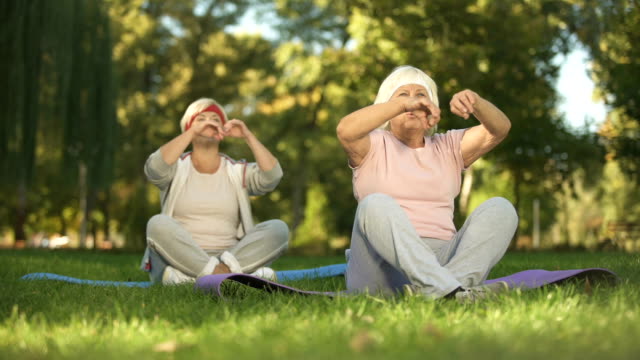 Elder-women-sitting-in-lotus-position-and-meditating-doing-yoga-in-park,-energy