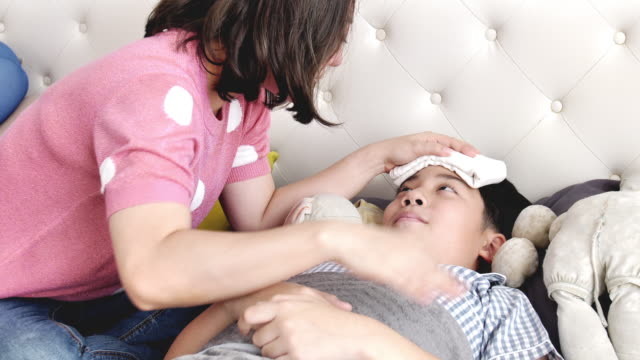 Asiatische-Kranken-jungen,-im-Bett-liegend,-Mutter-Überprüfung-seiner-Temperatur,-Slow-Motion-von-Mutter-und-Sohn-zu-Hause.
