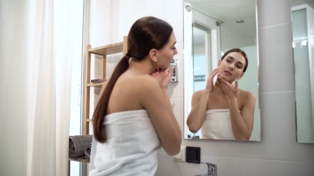 Skin-Care.-Woman-Touching-Face-And-Looking-At-Mirror-At-Bathroom