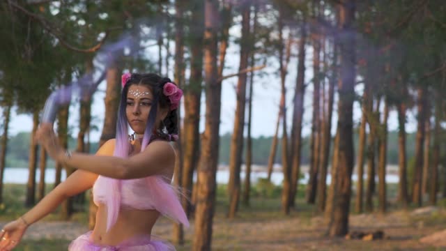 Pretty-girl-with-bright-makeup-in-a-pink-dress-dancing-with-smoke-bombs-outdoors.-The-dance-of-a-sensual-woman-with-a-flower-hairstyle.-Slow-motion.