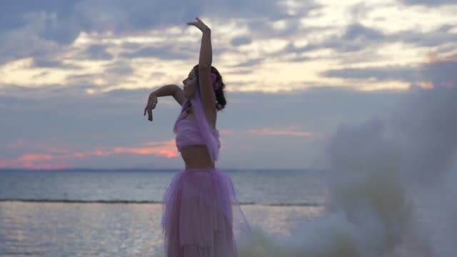 Beautiful-girl-with-bright-makeup-in-pink-dress-dancing-in-the-viscous-mist-from-smoke-bombs-outdoors.-The-dance-of-a-sensual-woman-with-a-flower-hairstyle.-Slow-motion.