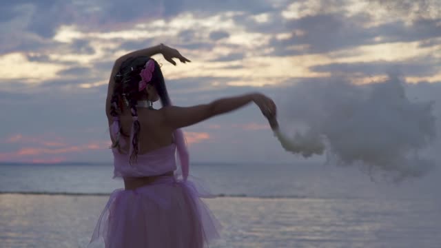 Beautiful-girl-with-bright-makeup-in-a-pink-dress-dancing-with-smoke-bombs-on-the-bank-of-the-river.-The-dance-of-a-sensual-woman-with-a-wonderful-hairstyle-with-flowers.-Slow-motion.