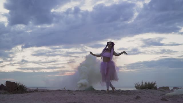 Beautiful-girl-with-sparkling-makeup-in-pink-dress-dancing-in-the-mist-from-smoke-bombs-on-the-bank-of-the-river.-The-dance-of-a-sensual-woman-with-a-flower-hairstyle.-Slow-motion.